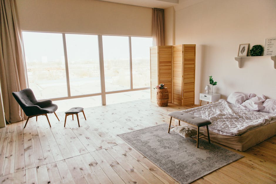 Elegant minimalist bedroom with wooden floors, large windows, and chic furniture, exuding a warm, inviting ambiance.